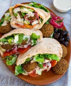 Pita broodjes gevuld met falafel, sla en saus op een bord, geserveerd met falafel kruidenmix.