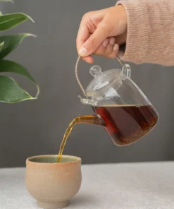 Hand schenkt zwarte Ceylon “UVA Highland” thee met cafeïne uit een glazen theepot in een kopje.