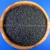 Houten kom gevuld met grof zeezout, Hawaii Zout Zwart – Black Lava, op een blauwe achtergrond.